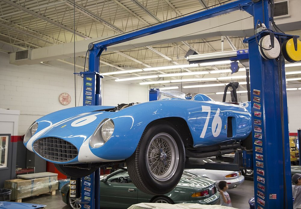A blue 1955 Ferrari sports racer raised on a two-post lift in a clean workshop
